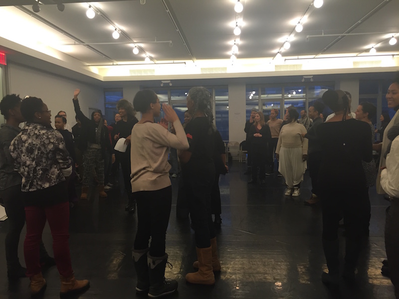 Women stand for a group exercise. One woman raises her hand.